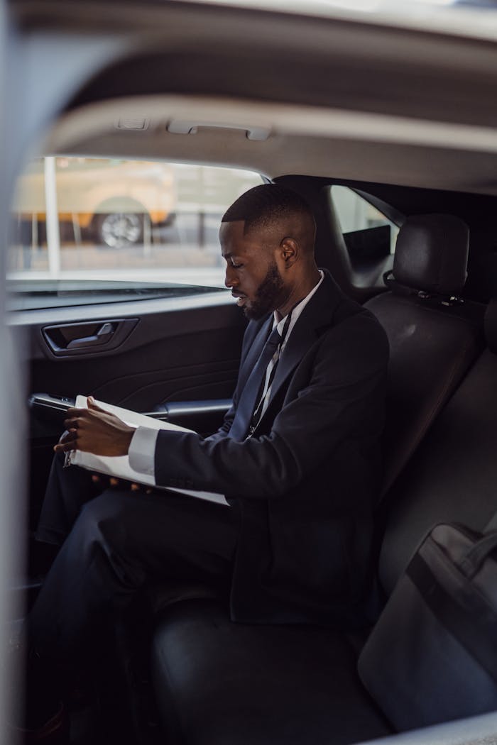 About A business professional in a suit reading documents inside a car.
