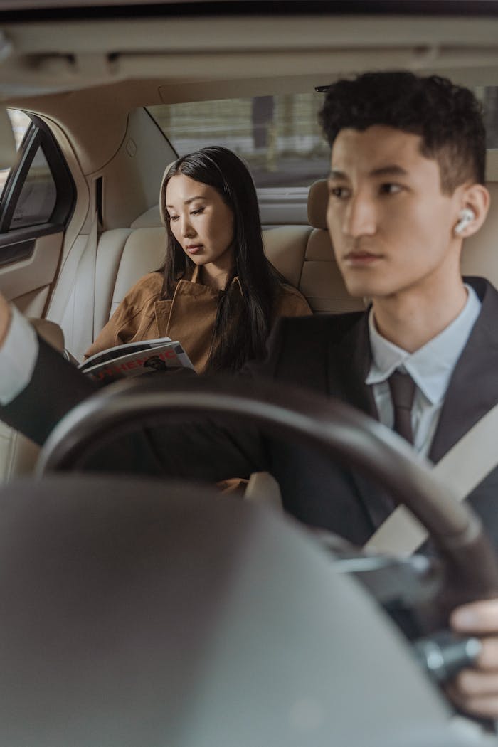 Mastering the First Impression: Your intriguing post title goes here A businessman driving a luxury car with a passenger reading, showcasing a serene and professional travel setting.