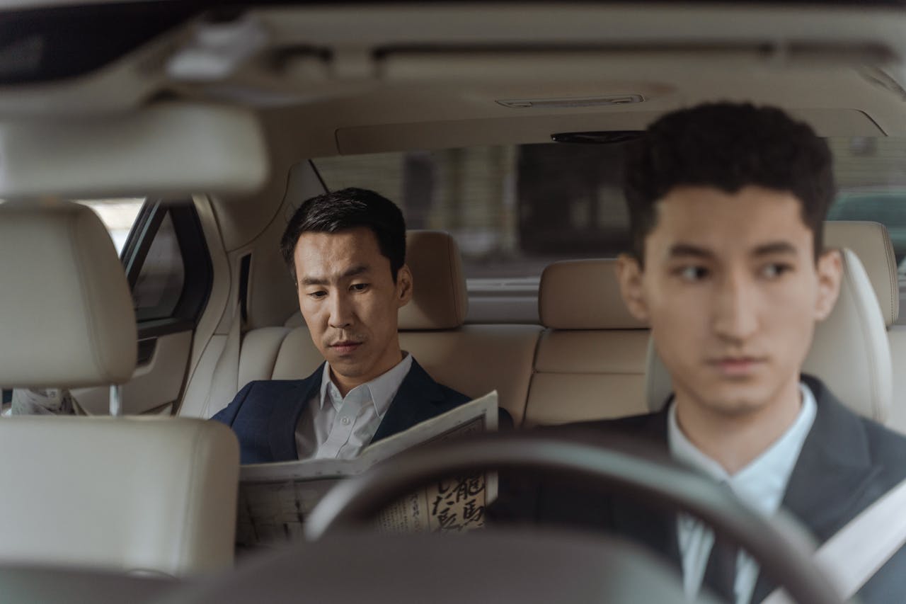 Services Elegant Asian businessman reading a newspaper inside a luxury car. Professional driver in focus.
